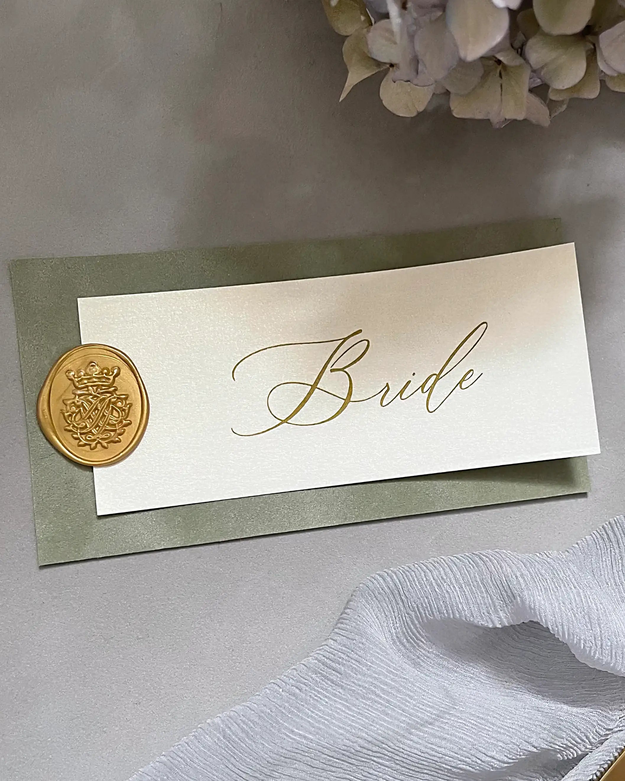A luxury wedding place card for the bride featuring a sage green French velvet base, transparent vellum overlay with gold foil calligraphy, and a gold wax seal — Polina Perri
